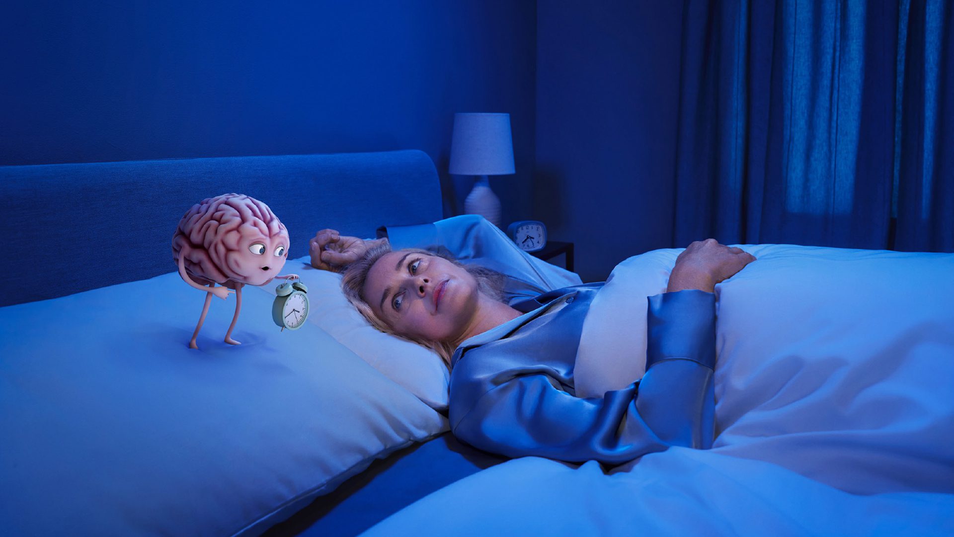 Campaign still sample Insomnia A blonde Caucasian women is in bed, arm above head wearing satin pyjamas. On the pillow a brain shaped character holds an alarm clock, and is looking at her whilst pointing to the clock